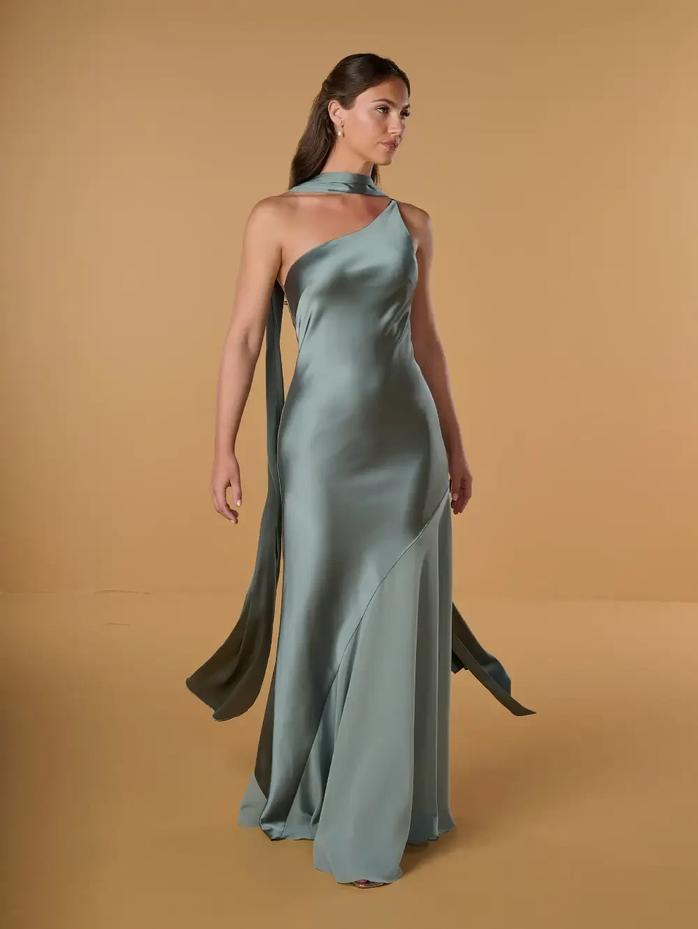 A model wearing a mint green satin dress with a one-shoulder design and flowing fabric.