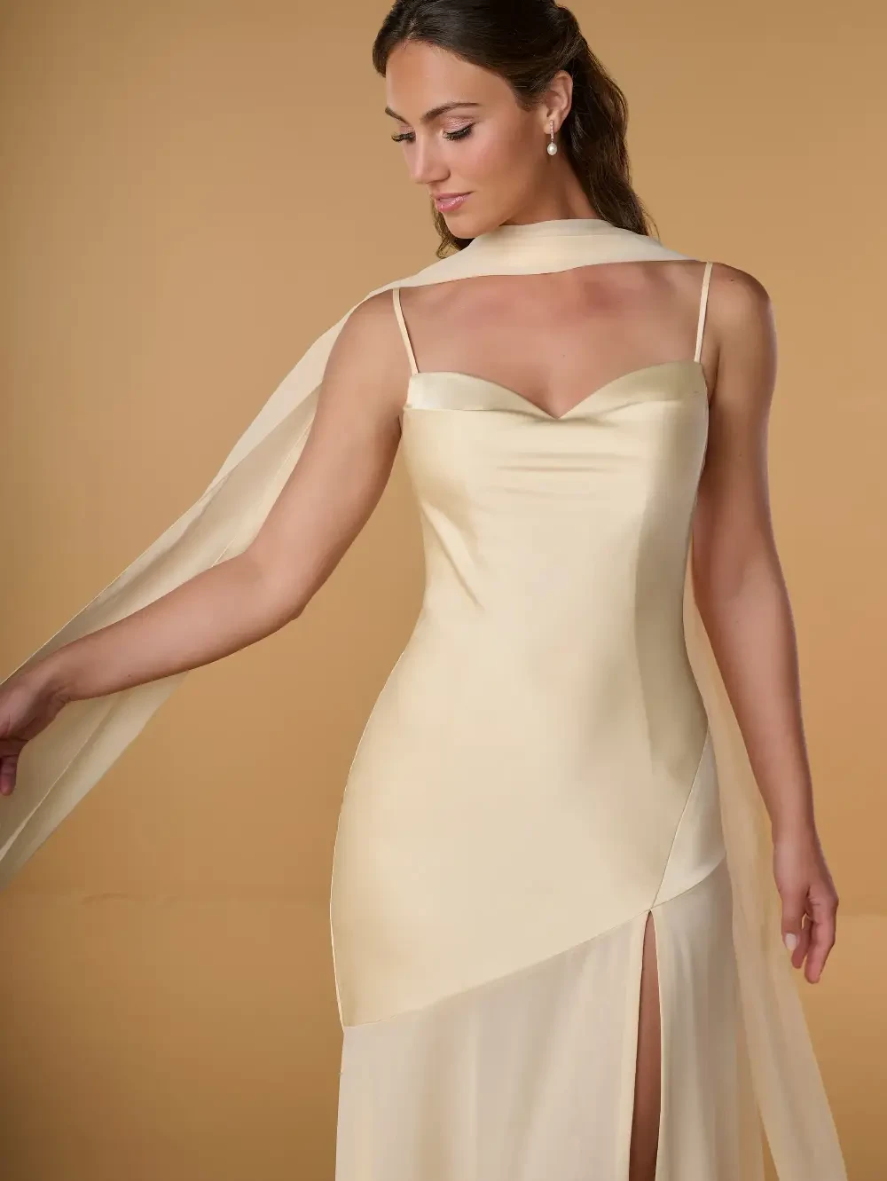A woman wearing a light yellow satin dress with a thigh-high slit and a flowing scarf-like detail.