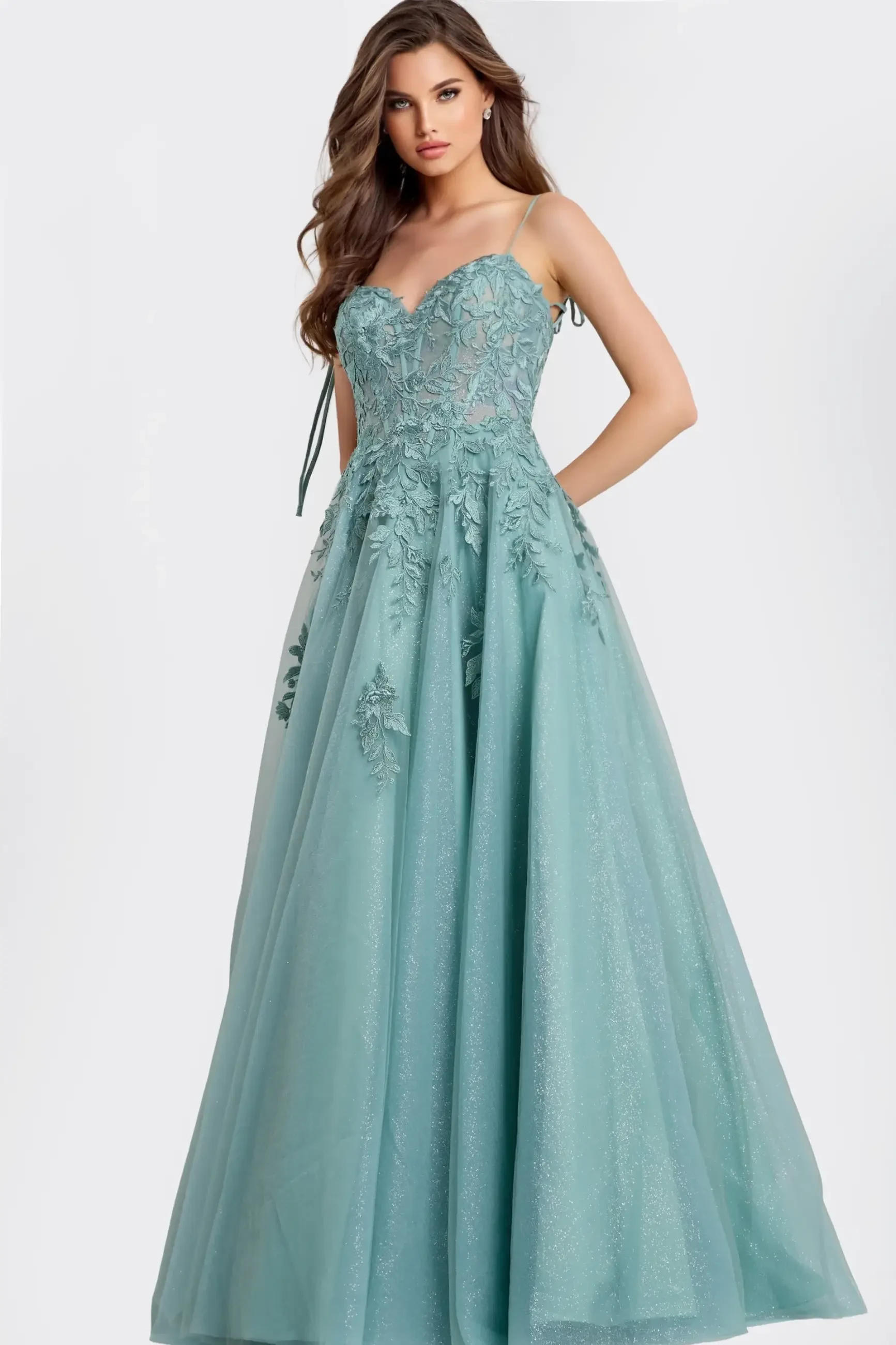 Woman in a light blue, elegant ball gown with floral lace details and thin straps. She poses confidently against a soft white background. The mood is graceful and sophisticated.