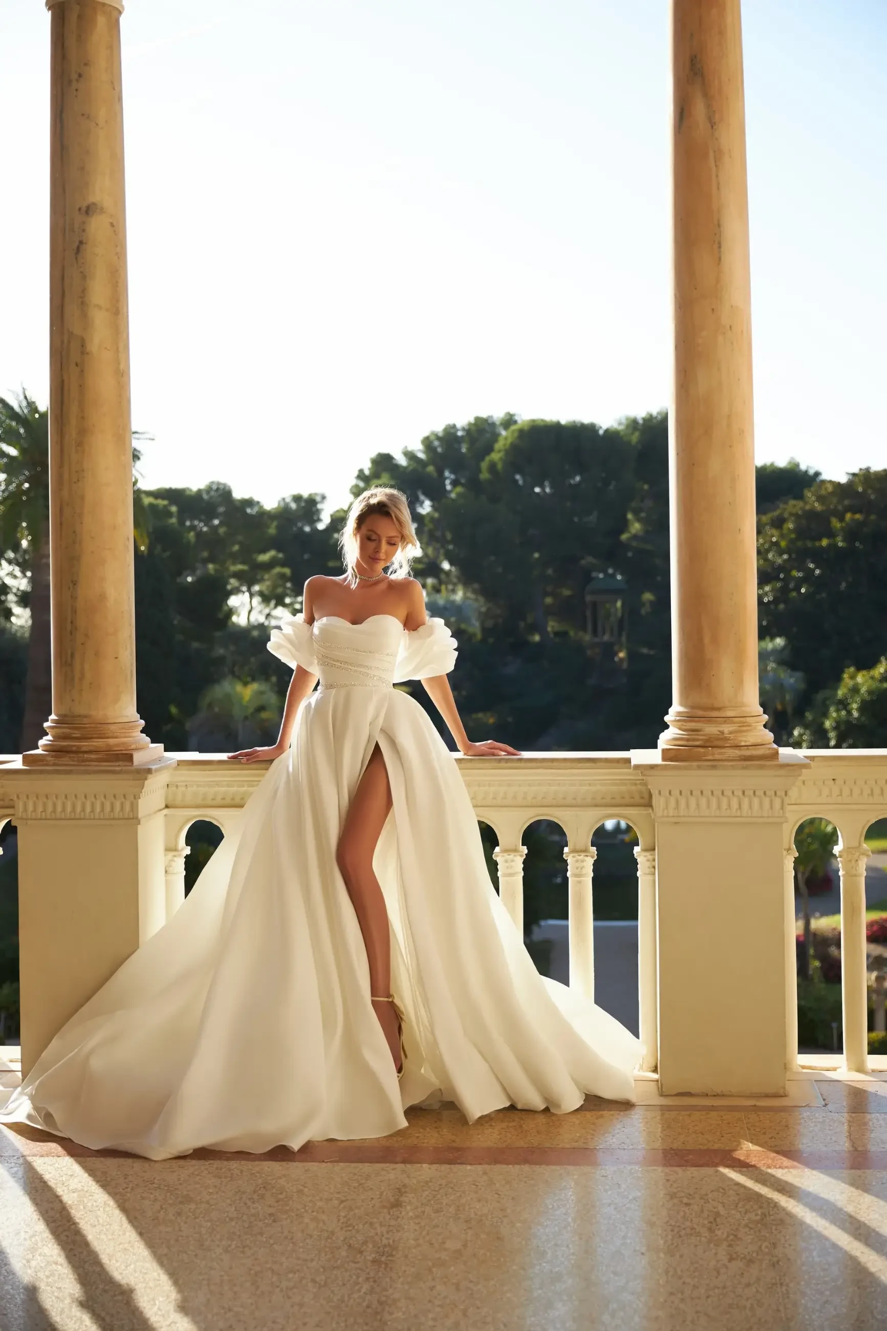 model is wearing an off the shoulder ball gown wedding dress with a slit