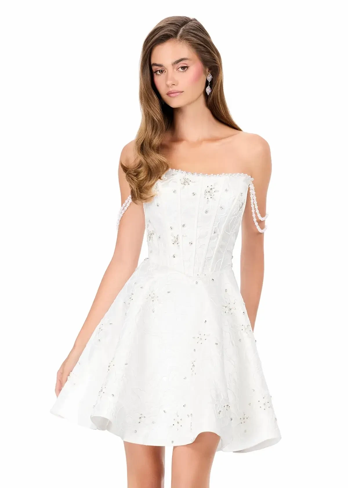 A young woman in a strapless white dress adorned with embellishments, standing confidently and looking at the camera.